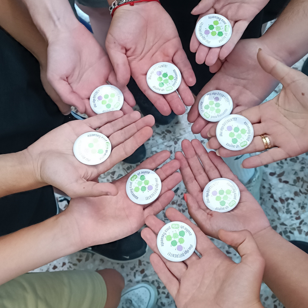 Manos de niños sujetando chapas con el logotipo del proyecto Asume un reto poco frecuente