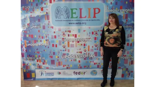 María Tudela, presidenta de AELIP, posando frente al cartel de la asociación.